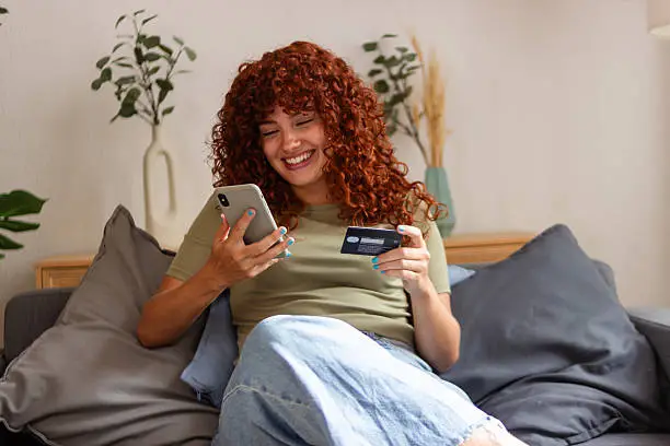 Mujer realizando una compra digital a través del teléfono móvil, sujetando una tarjeta bancaria.